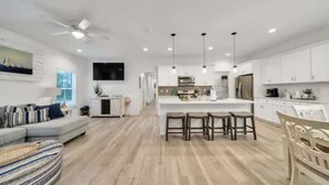 A modern kitchen with white cabinets, a central island with stools, and pendant lighting. - Hot tub, The Tiki Hideaway, Close to Bay & Beach, Backyard Tiki Bar, Paddleboards (Santa Rosa Beach)
