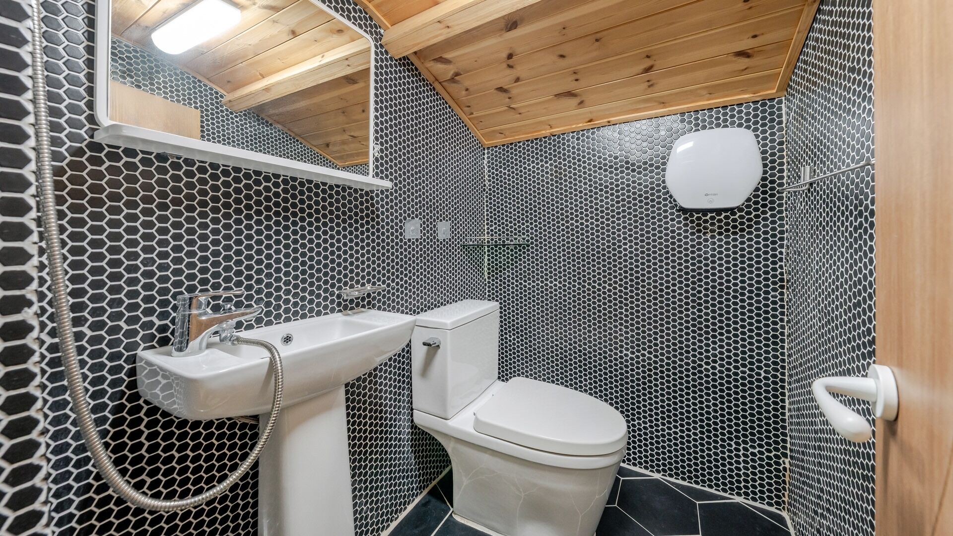 Um banheiro com padrão de azulejos hexagonais, pia branca, vaso sanitário e teto de madeira.