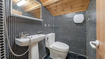 Um banheiro com padrão de azulejos hexagonais, pia branca, vaso sanitário e teto de madeira.