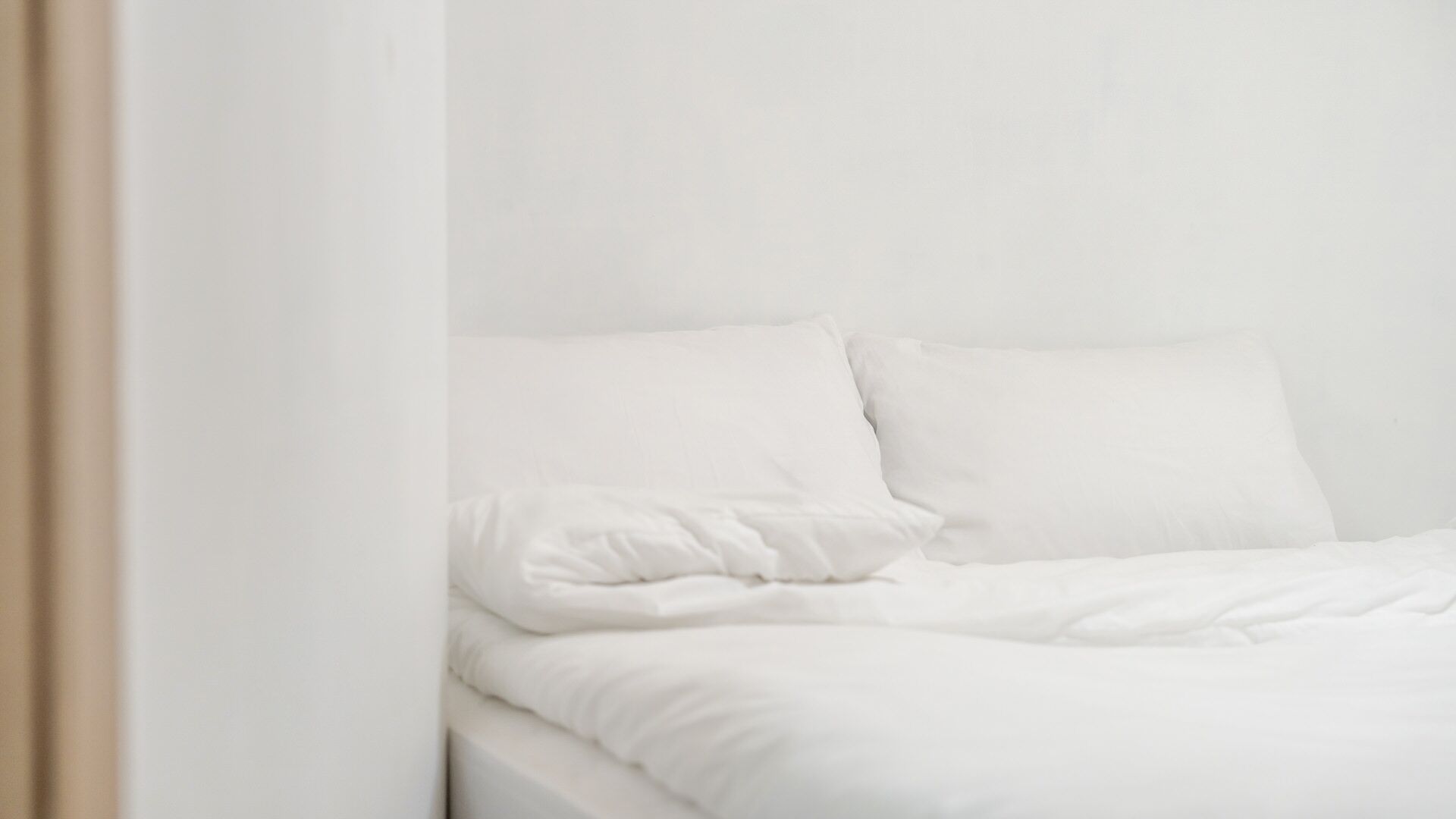 A bed with white bedding in a room with white walls.