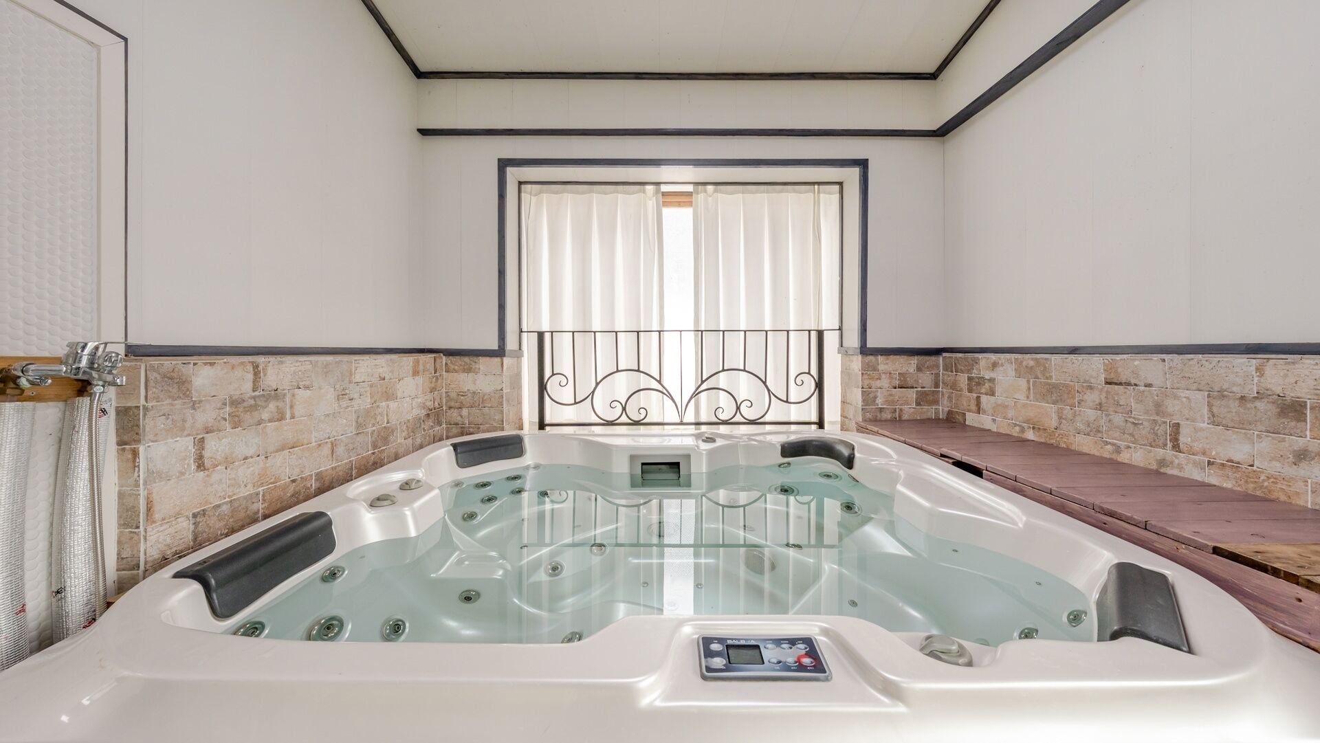 A spa room with a hot tub, stone wall, and a window with curtains.