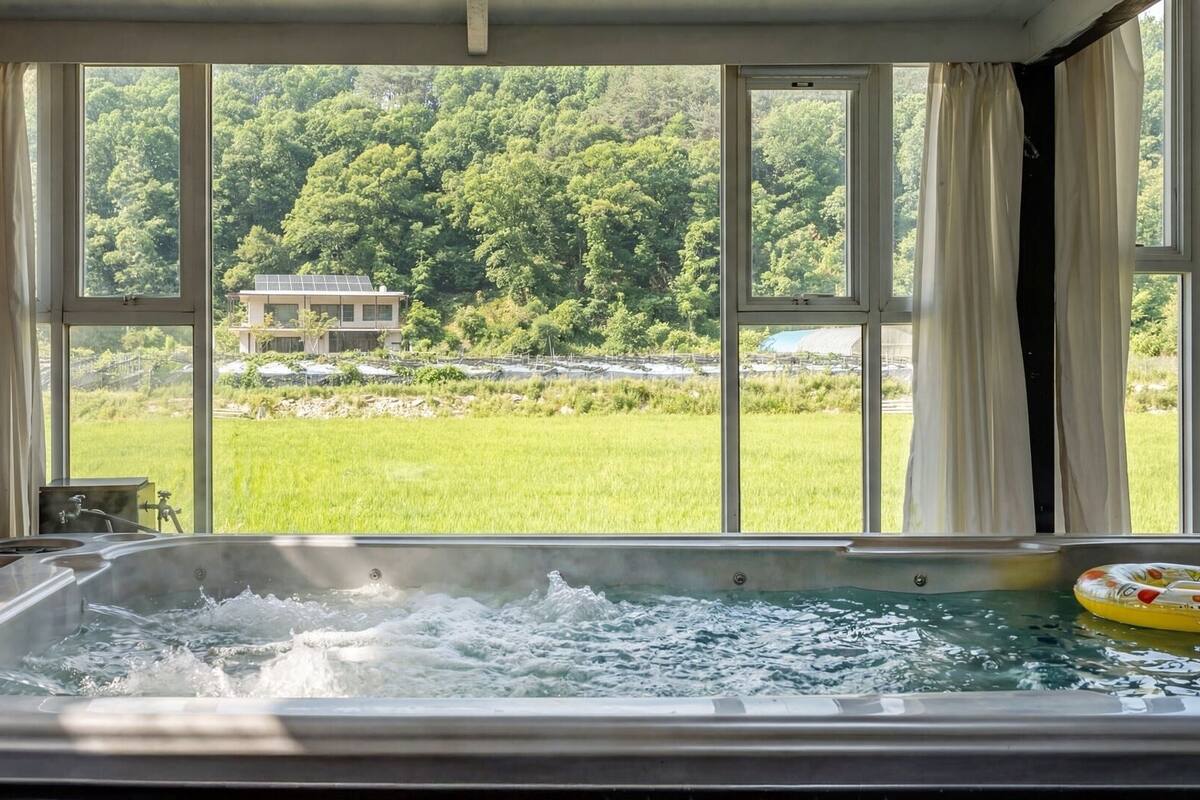 Ein Whirlpool mit Blick auf ein grünes Feld und Bäume durch große Fenster.