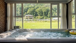 A hot tub with a view of a green field and trees through large windows. - Goesan Glam House Pet Pension (Goesan)