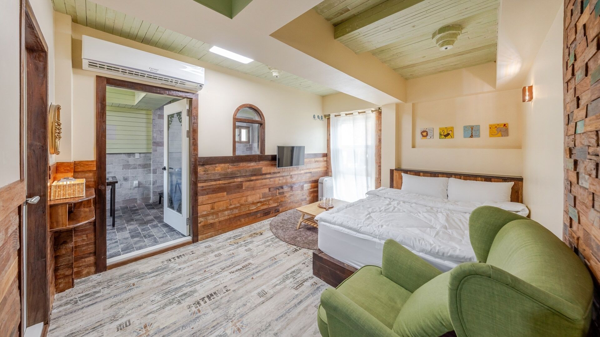 A bedroom with a bed, a green armchair, a wooden wall, a television, and a bathroom with a shower and a toilet.