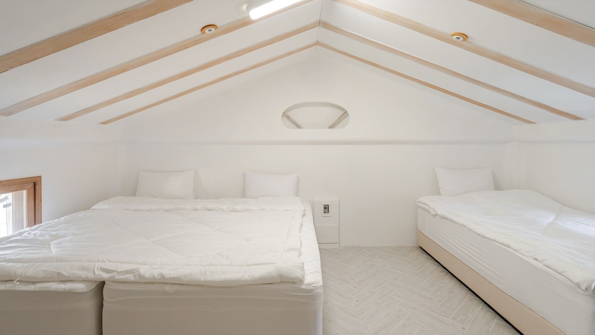 Un dormitorio con techo inclinado, dos camas, una lámpara y un enchufe.
