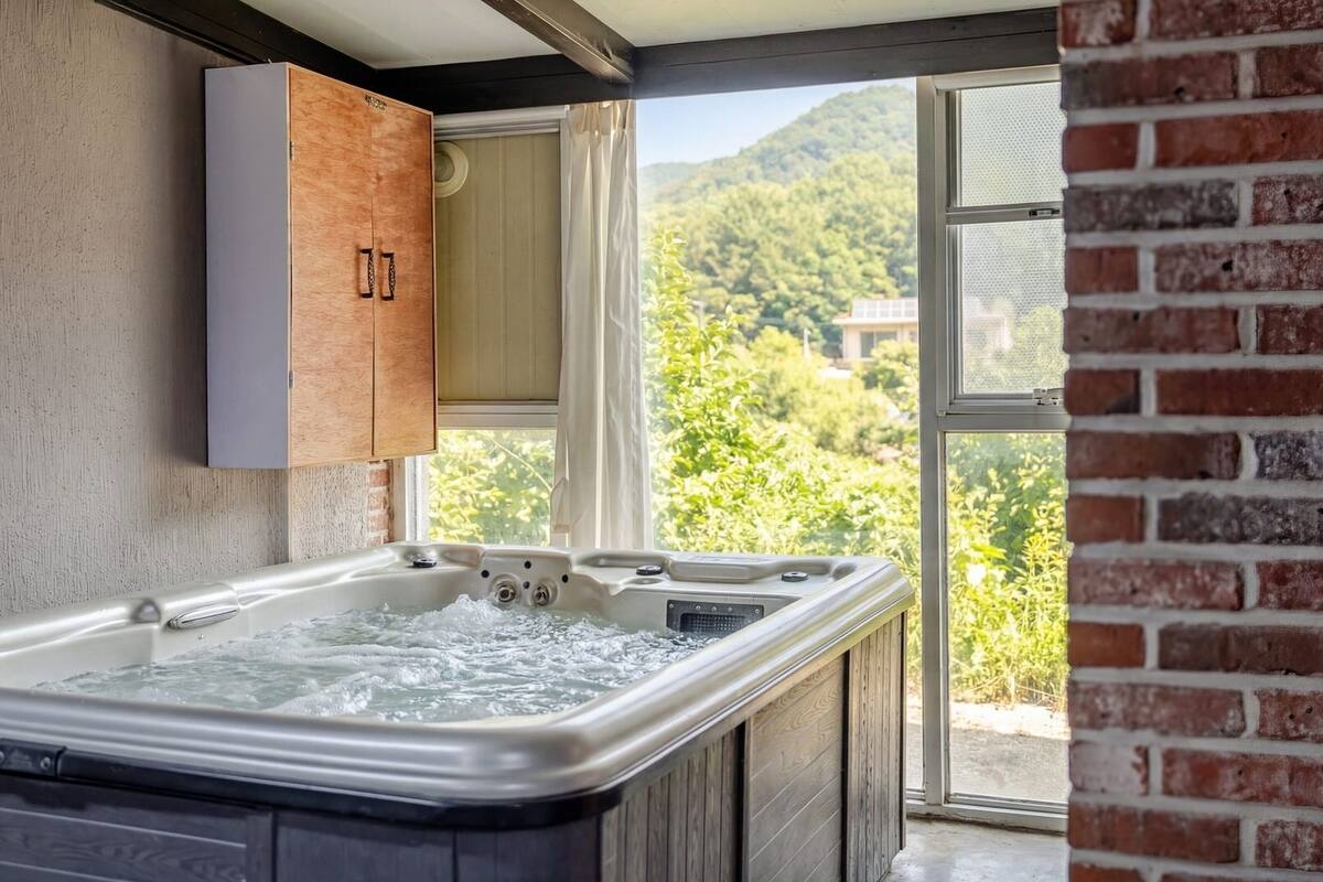 Ein Wellnessbereich mit Whirlpool, Holzschränken und Blick auf eine grüne Landschaft durch ein großes Fenster.