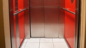 An elevator with metallic doors and red accents, featuring a handrail on one side. - Hotel Cityring (Frankfurt)