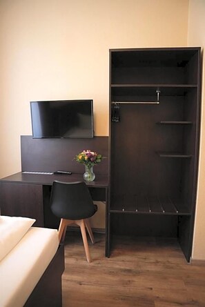 Una habitación de hotel con una cama, un escritorio con silla, un televisor y un armario.