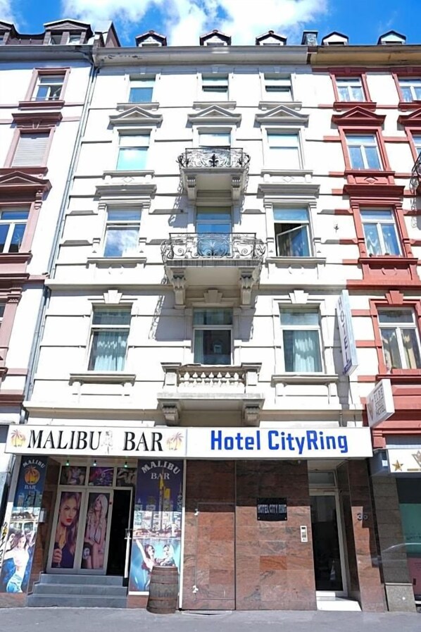 Un edificio con letreros que indican 'Malibu Bar' y 'Hotel CityRing', exhibiendo un estilo arquitectónico clásico con numerosas ventanas y balcones.