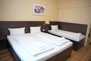Habitación de hotel con una cama grande, una cama más pequeña y un banco. Hay una lámpara de pared y un cuadro enmarcados en la pared.