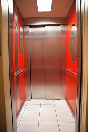 A modern elevator with metallic doors and red accents, featuring a tiled floor and a skylight above. - Hotel Cityring (Frankfurt)