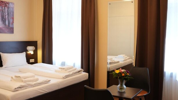 A hotel room with a bed, a desk with chairs, a mirror, and a window with curtains. - Hotel Cityring (Frankfurt)