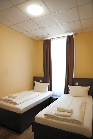 A hotel room with two single beds, a window with curtains, and a ceiling light. - Hotel Cityring (Frankfurt)