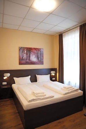 Habitación de hotel con una cama grande, dos mesitas de noche, un cuadro en la pared y una ventana con cortinas.