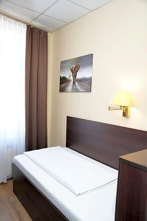 A hotel room with a bed, a wall-mounted lamp, a painting, and a window with curtains. - Hotel Cityring (Frankfurt)