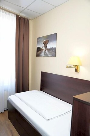 Habitación de hotel con cama, lámpara de pared, un cuadro y ventana con cortinas.