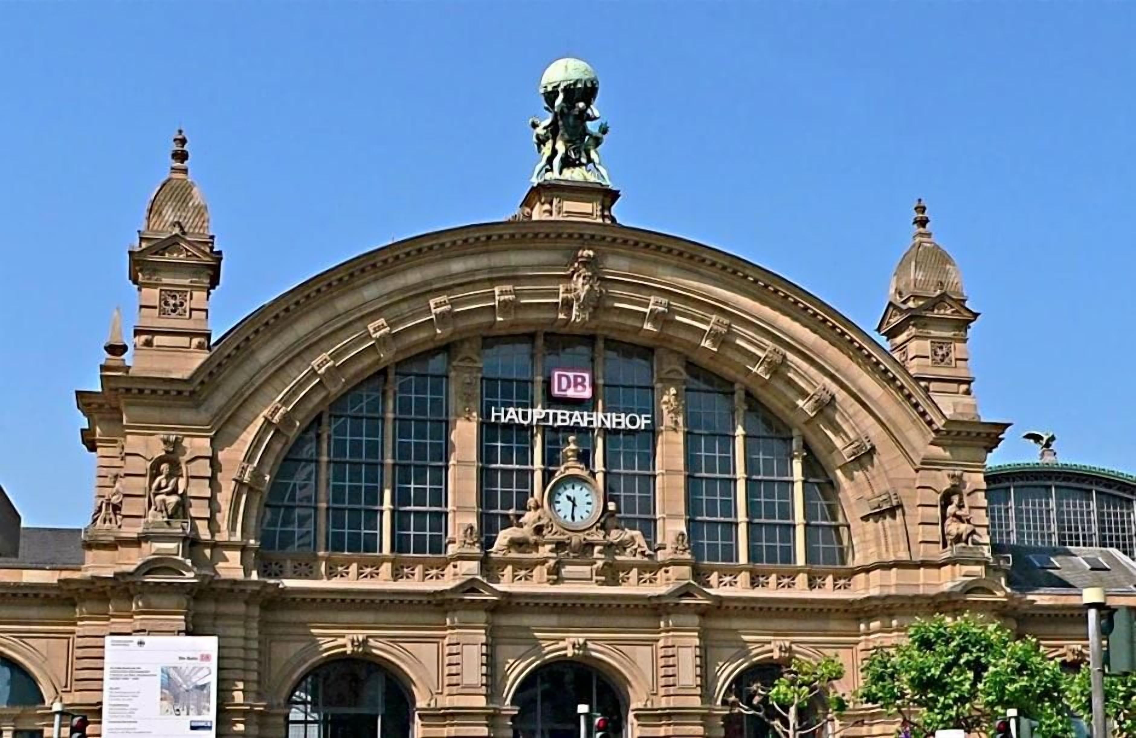 A historic building with a large clock, ornate sculptures, and a sign reading 'DB Hauptbahnhof'.