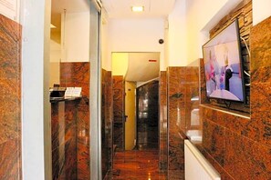 A hallway with marble walls, a glass door, and a mounted television. - Hotel Cityring (Frankfurt)