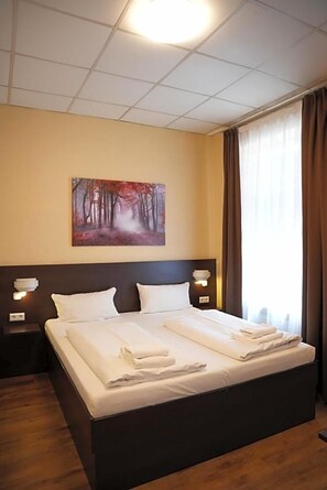 A hotel room with a large bed, two bedside tables, a painting on the wall, and a window with curtains. - Hotel Cityring (Frankfurt)