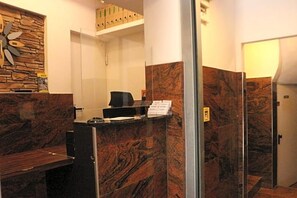 Una zona de recepción con mostrador de mármol, un reloj en la pared y una escalera que lleva a un nivel superior.