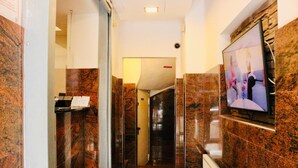 A hallway with marble walls, a glass door, a mounted TV, and a visible door leading to another room. - Hotel Cityring (Frankfurt)