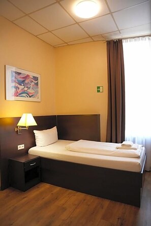 A hotel room with a single bed, a nightstand, a wall-mounted lamp, and a painting. - Hotel Cityring (Frankfurt)