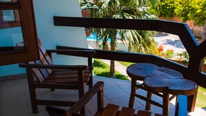 A covered outdoor seating area with wooden furniture and a view of greenery. - Vila Mundaí – Peace and quiet, 500m from the beach. (Porto Seguro)