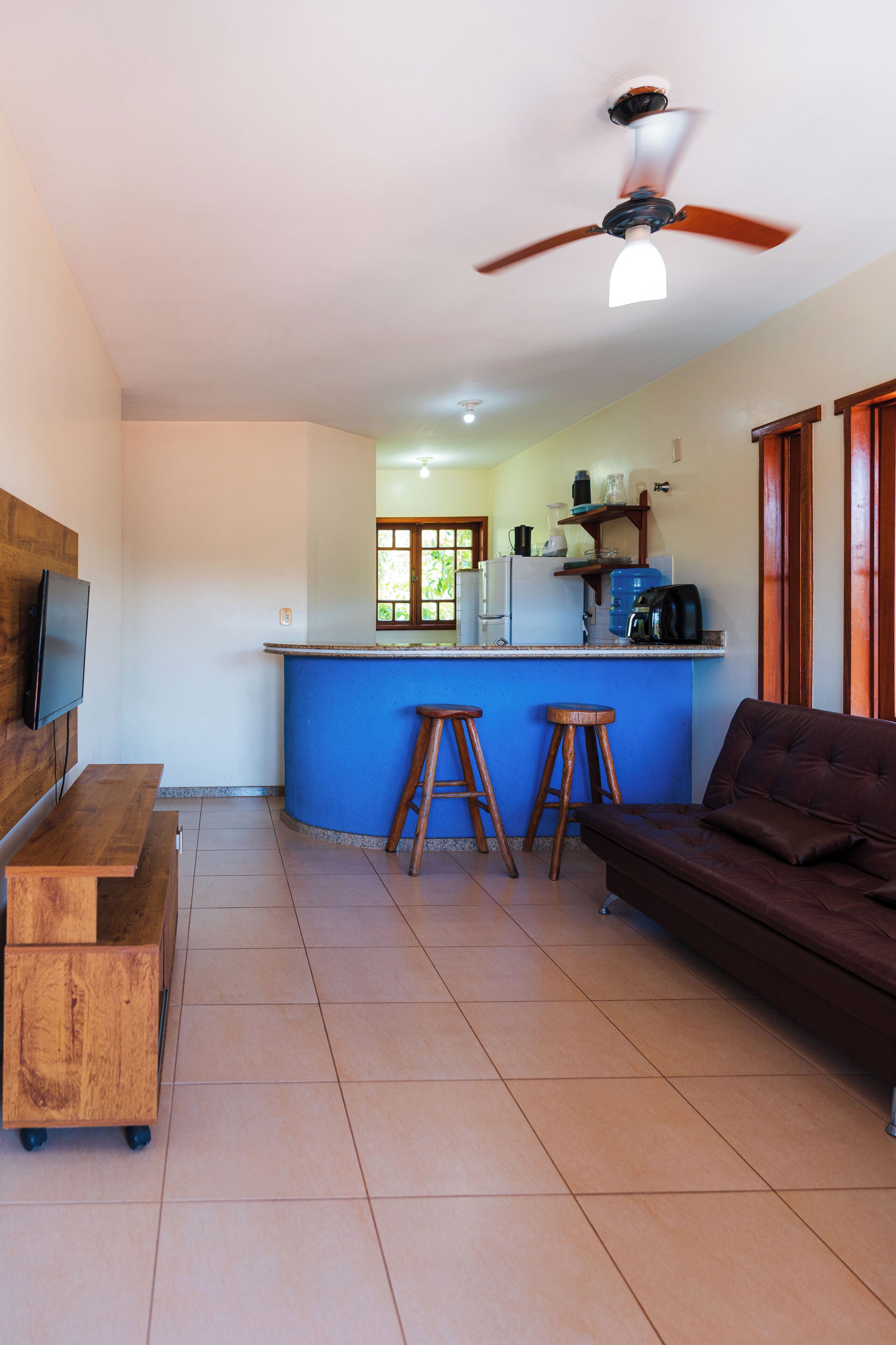 A compact living space with a kitchenette, a ceiling fan, a television, and a sofa.