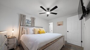 Un dormitorio con cama, mesita de noche, cómoda, ventilador de techo y puerta.