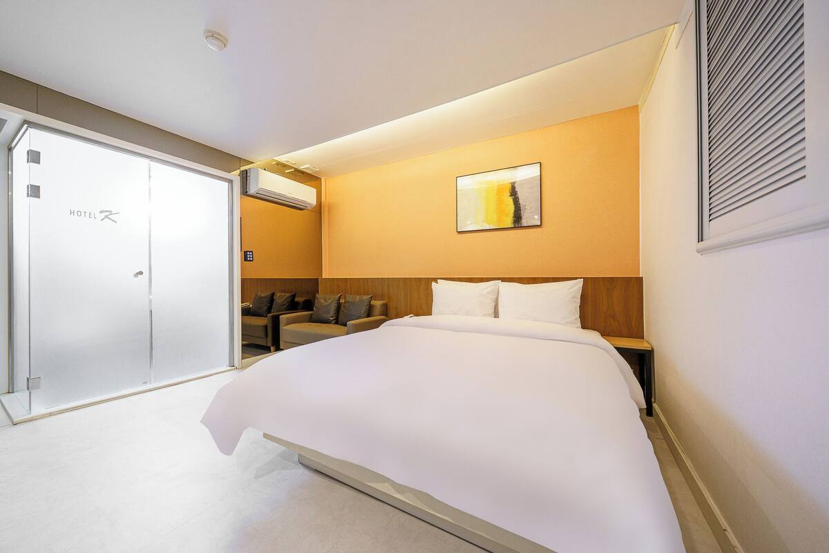 Una camera d'albergo con un letto grande, un divano, un'opera d'arte appesa al muro e una porta scorrevole.