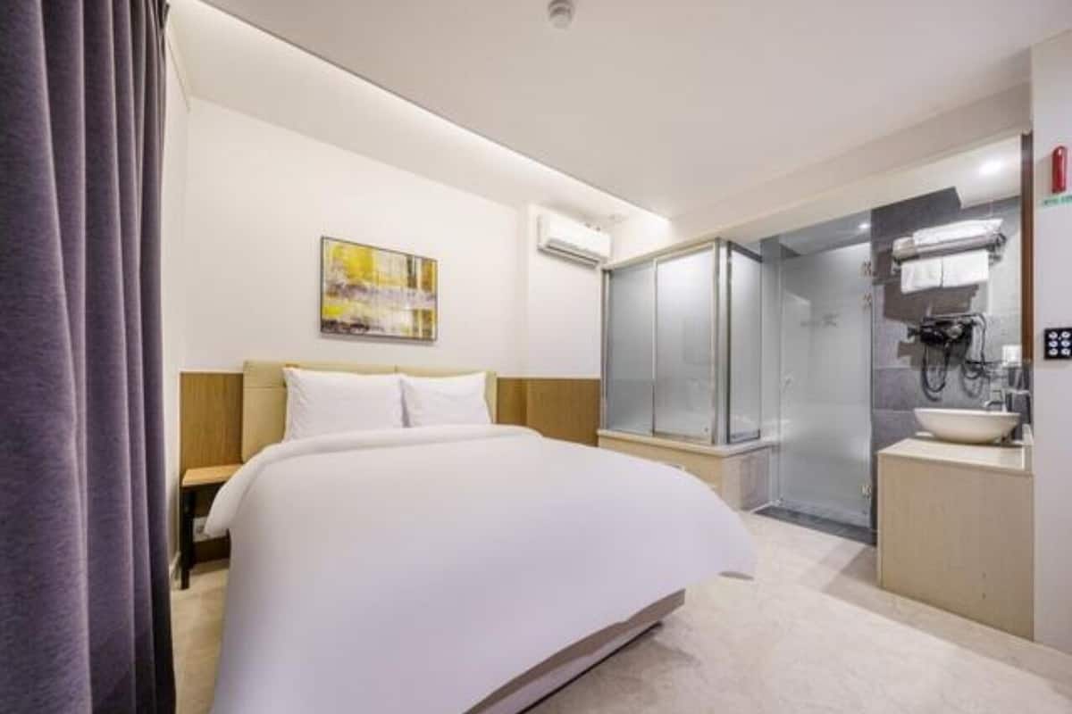 Una camera d'albergo con un letto, una doccia, un lavandino e un quadro appeso al muro.