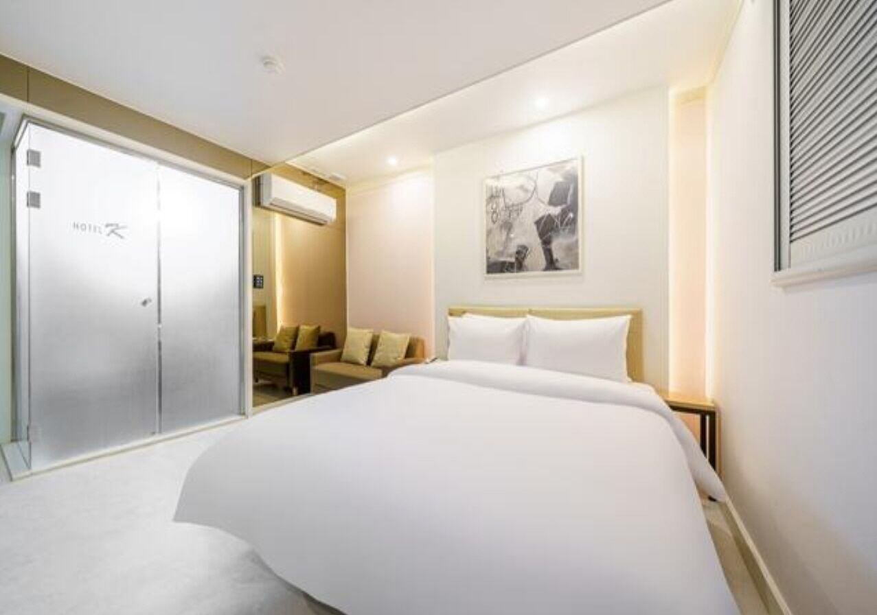 Quarto de hotel com uma cama grande, um guarda-roupa, um sofá e uma obra de arte emoldurada na parede.