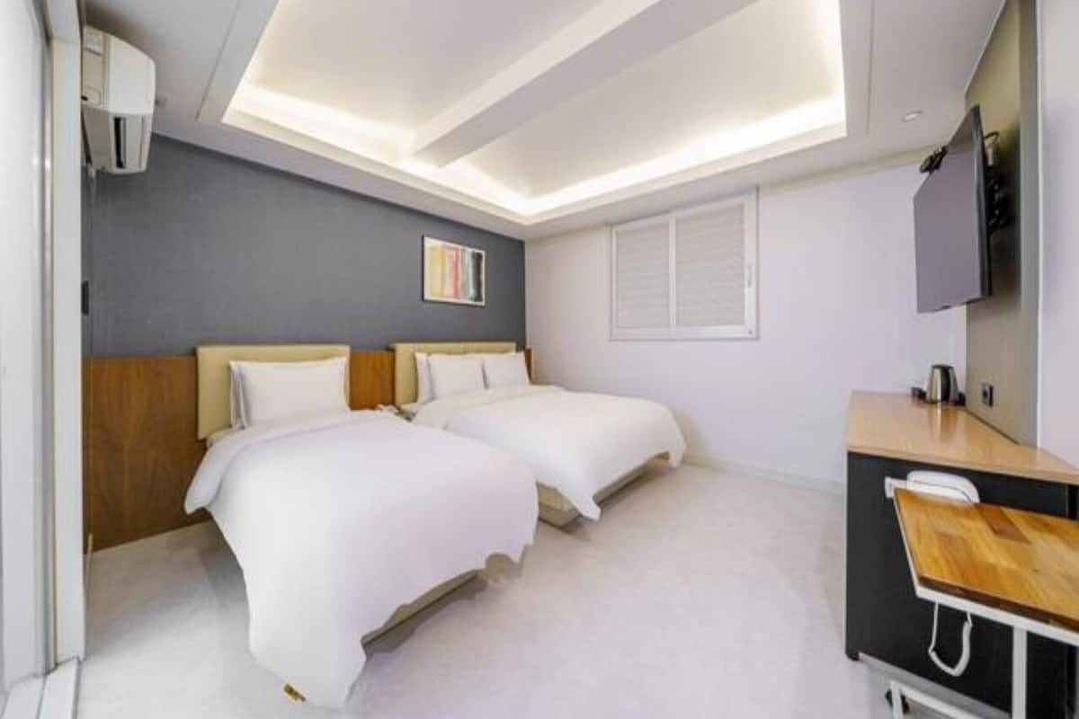 Una camera d'albergo con due letti, una scrivania, una televisione e una finestra.