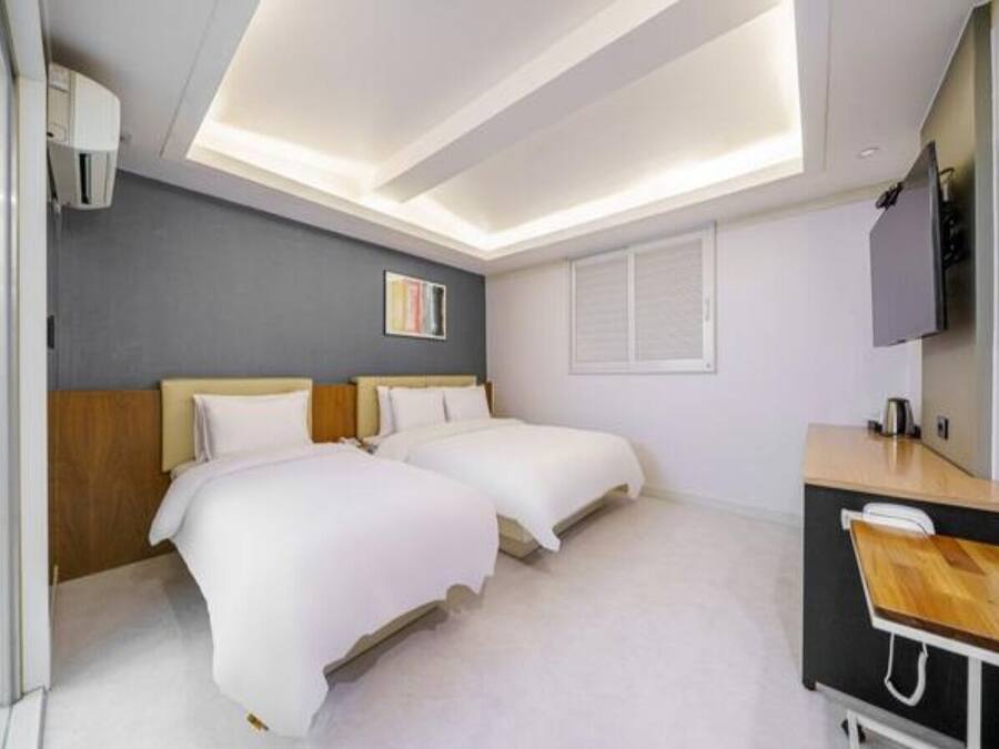 A hotel room with two beds, a desk, a TV, and a window.