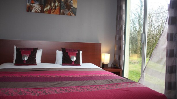 A hotel room with a large bed, a painting on the wall, and a window with a view of trees. - Latitude Ouest Hotel Restaurant Spa (Locronan)