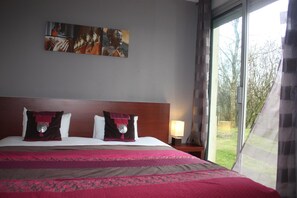 A hotel room with a large bed, a painting on the wall, and a window with a view of trees. - Latitude Ouest Hotel Restaurant Spa (Locronan)