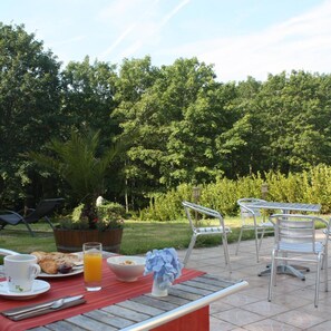 An outdoor dining area with metal chairs and a table, surrounded by lush greenery and trees. - Latitude Ouest Hotel Restaurant SPA (Locronan)