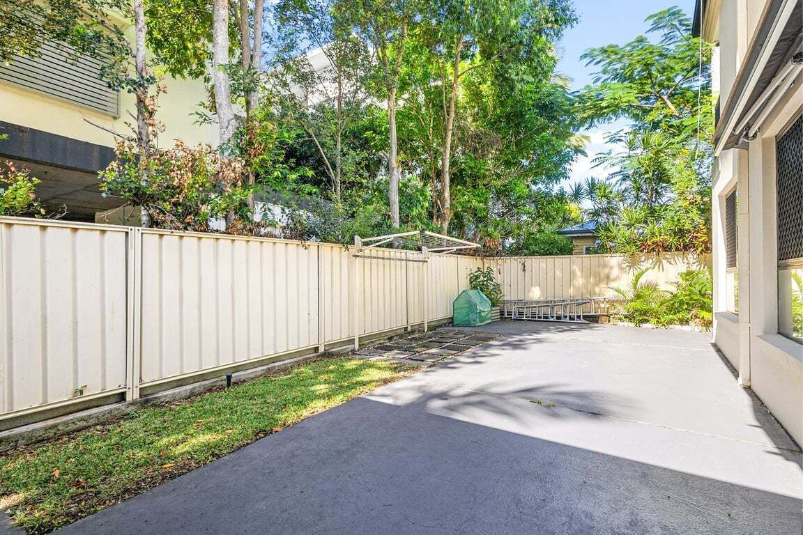 En baghave med en beton terrasse, et træhegn og et lille haveområde.