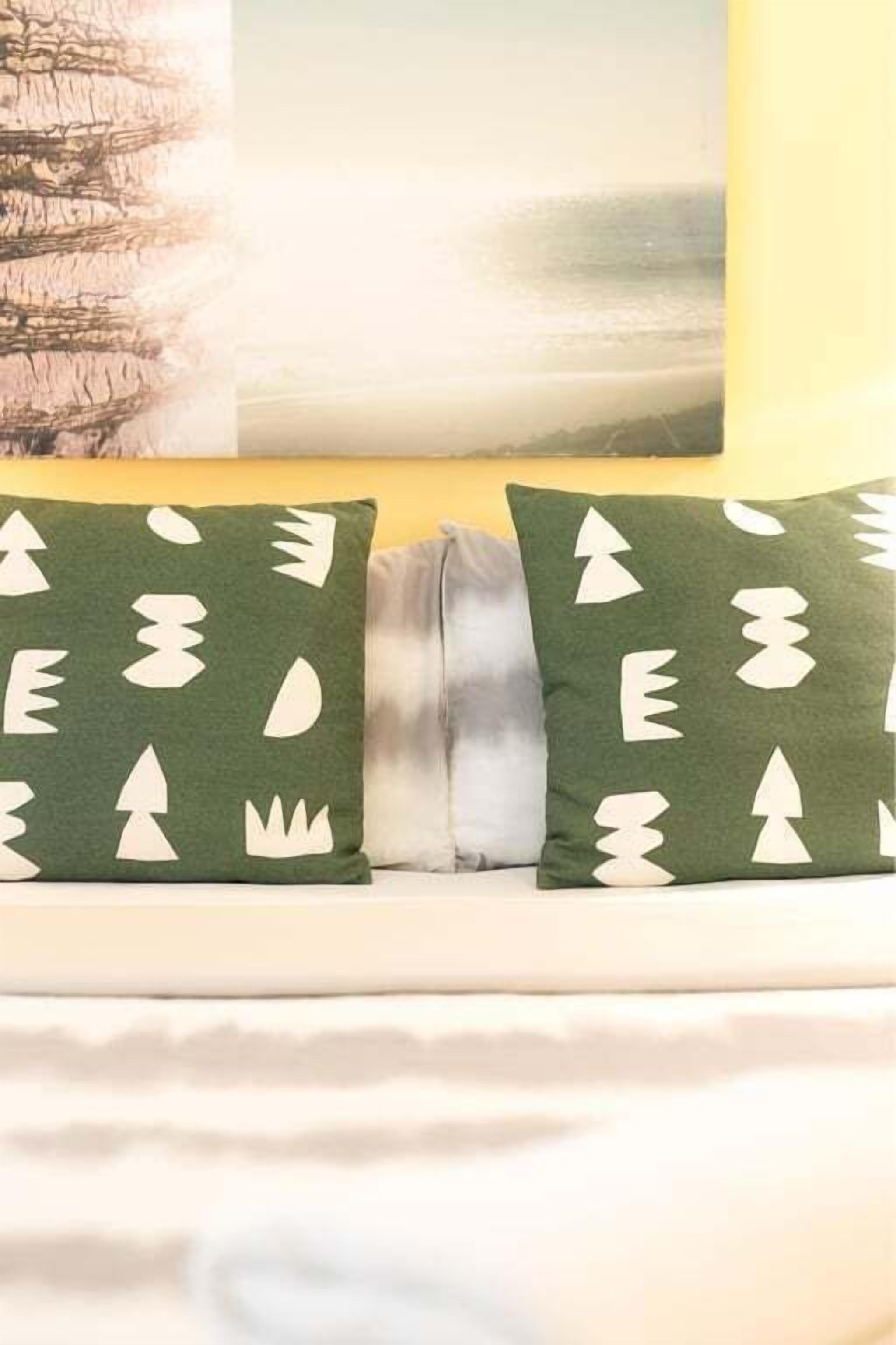 A bed with two pillows featuring a tree pattern, a painting of a landscape, and a yellow wall.