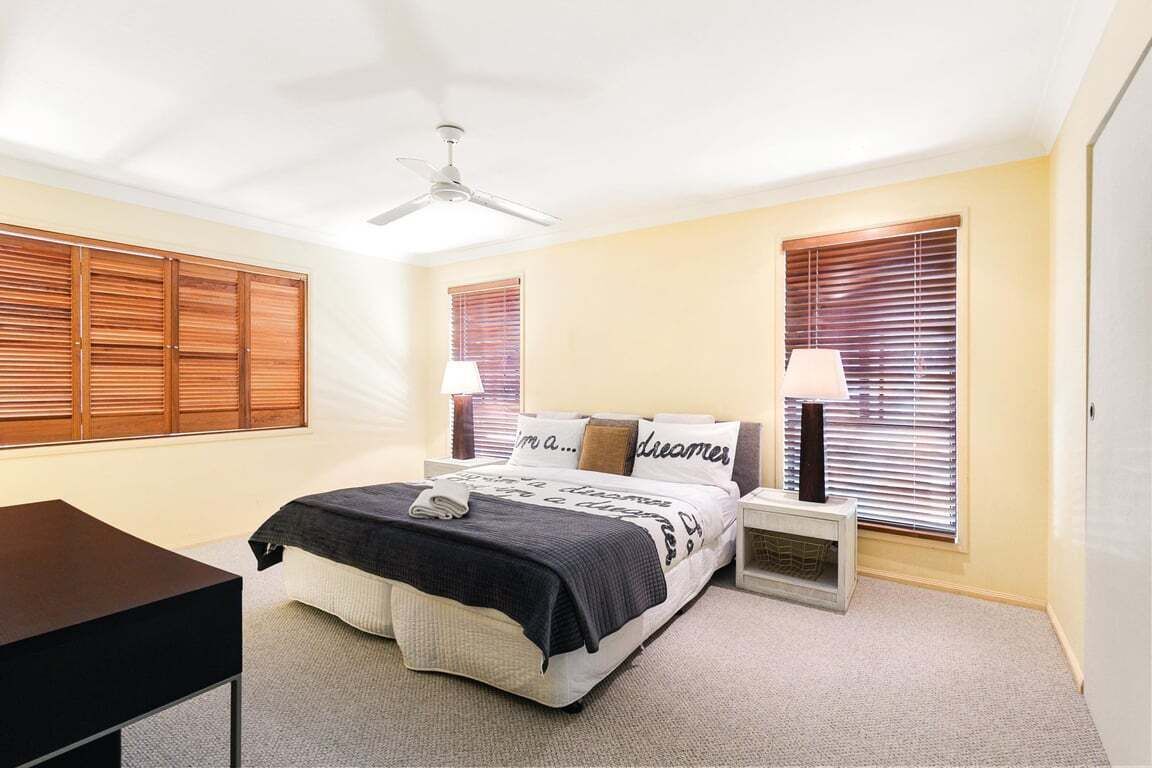 A bedroom with a bed, bedside tables, a ceiling fan, and a heater.