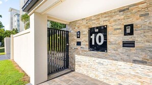 Ein moderner Gebäudeeingang mit steinverkleideter Fassade, einem schwarzen Tor und einem Schild mit der Nummer 10.