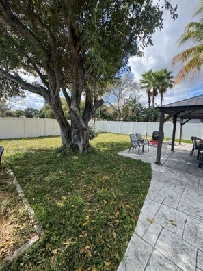 Eine Terrassenfläche mit einer Pergola, Gartenmöbeln und einem großen Baum.