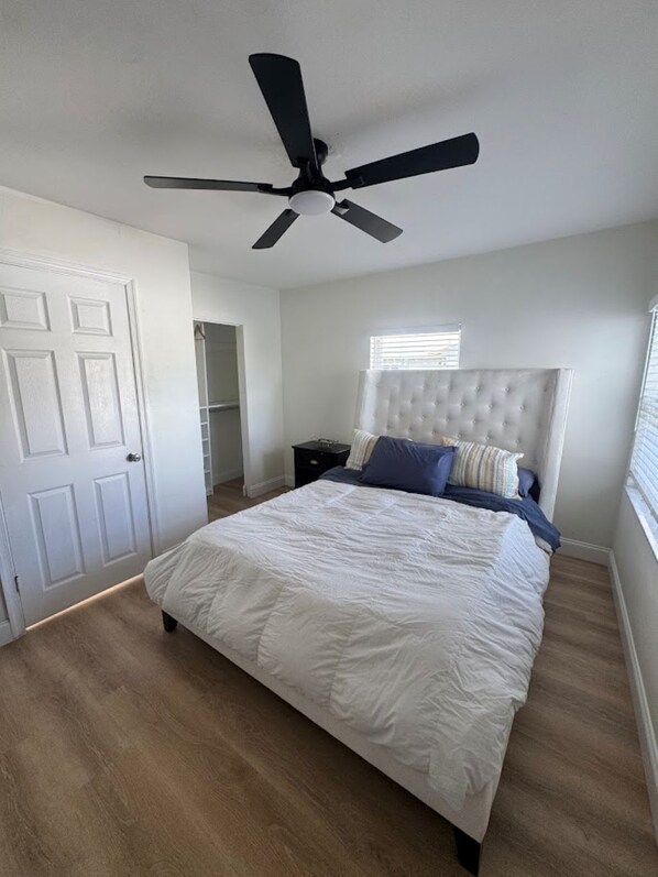 Ein Schlafzimmer mit Bett, Deckenventilator, Fenster und Tür.