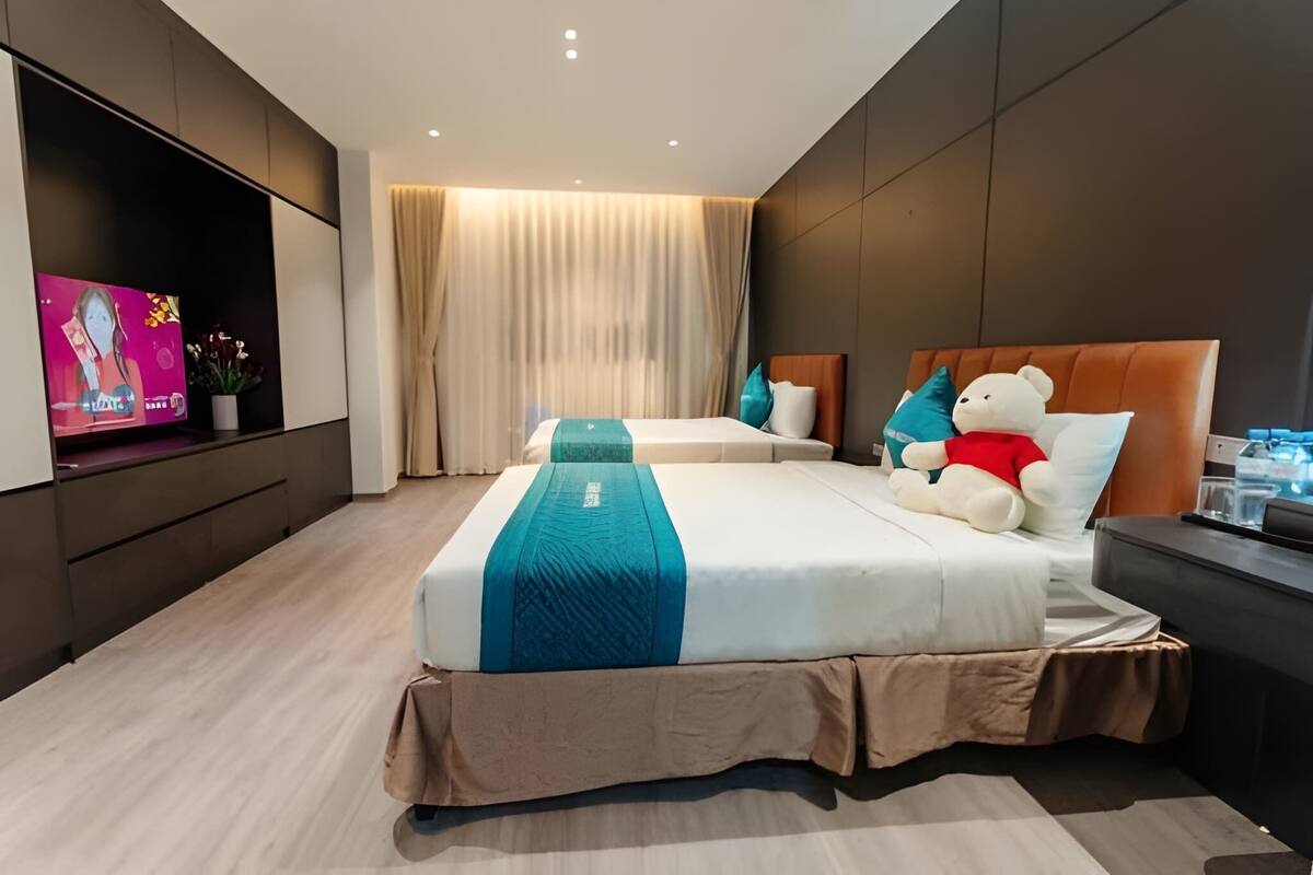 Ein modernes Hotelzimmer mit einem großen Bett, einem Fernseher an der linken Wand und einem Nachttisch mit einem Teddybär.