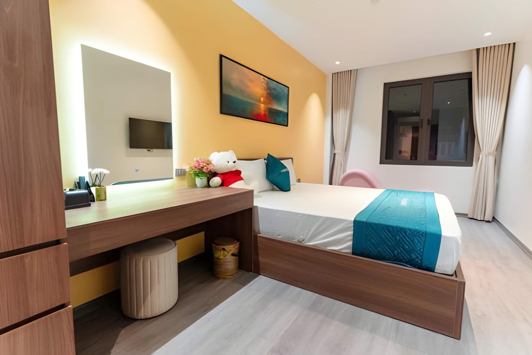 Hotelkamer met een bed, een bureau met stoel, een televisie, een raam en een schilderij aan de muur.