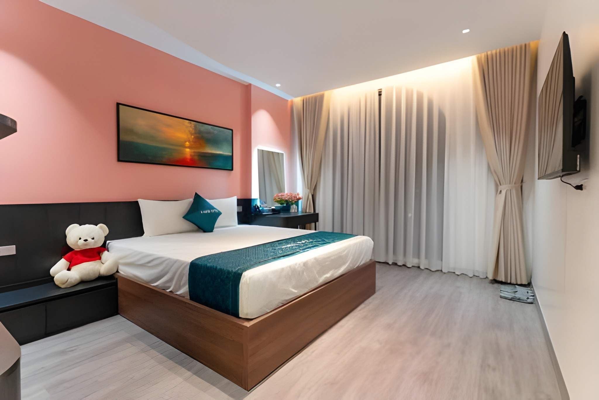 Een moderne slaapkamer met een groot bed, een nachtkastje, een stoel, een teddybeer, een schilderij, een televisie en gordijnen.