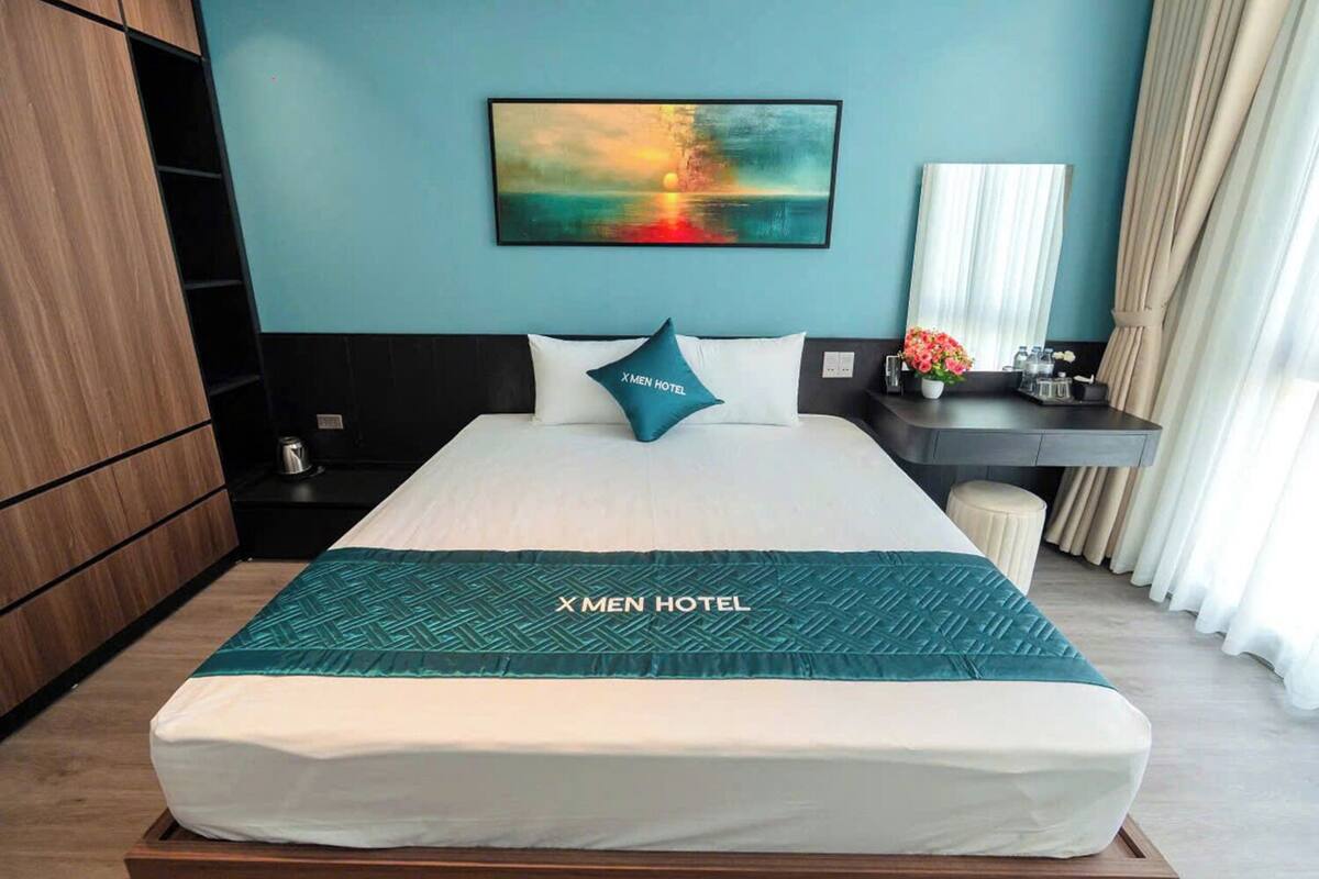 Ein Hotelzimmer mit Bett, einem Bild an der Wand, einem Schreibtisch und einem Nachttisch.