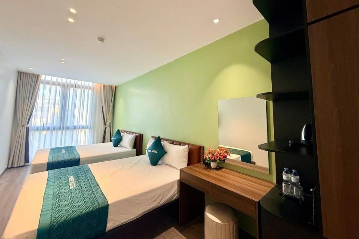 Ein Hotelzimmer mit zwei Betten, einem Schreibtisch, einem Spiegel und einer Mülleimer.