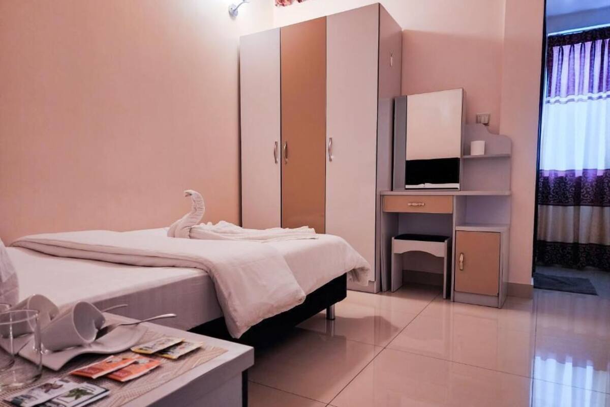 A hotel room with a bed, a desk with a chair, a wardrobe, and a television.
