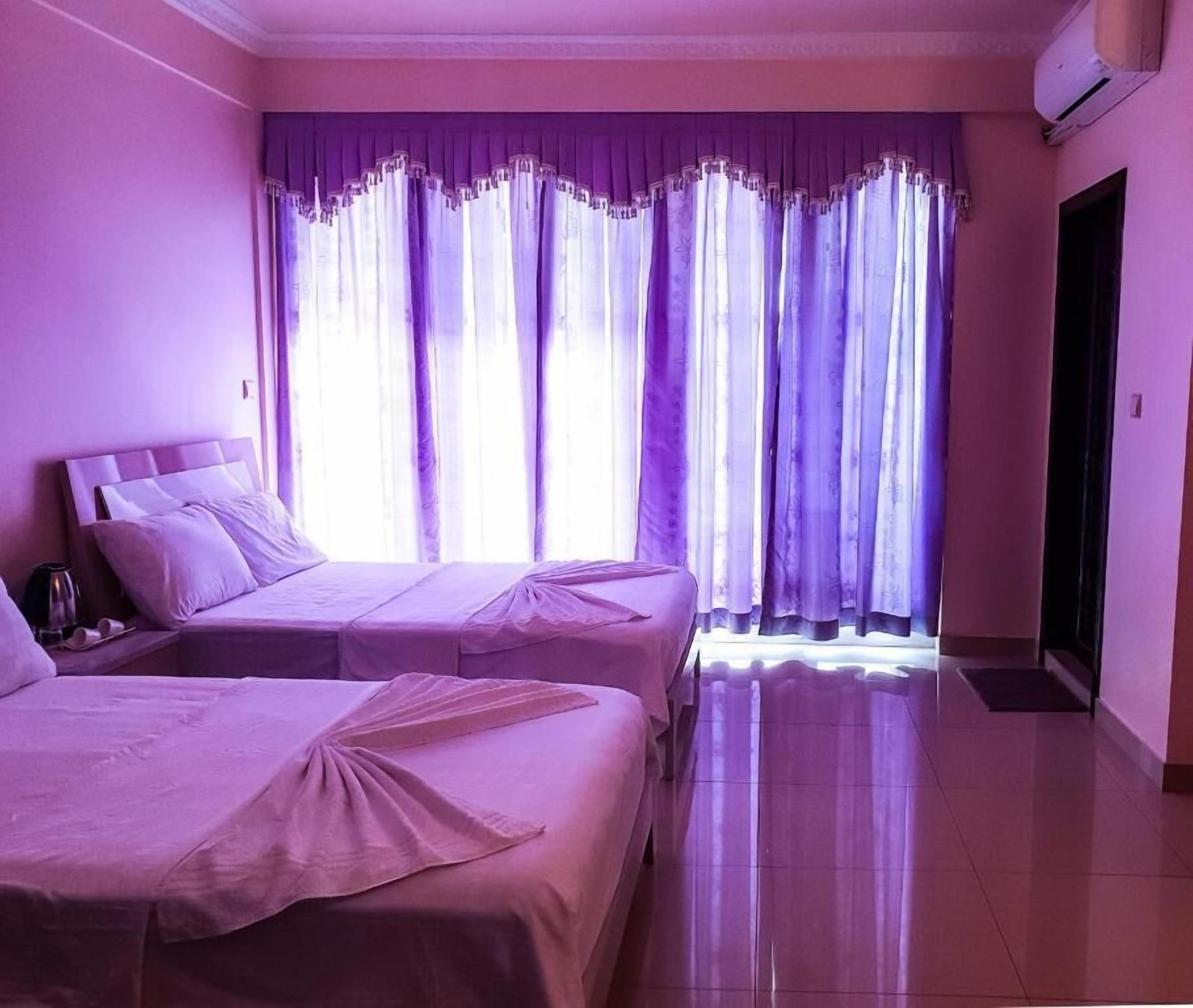 Een kamer met twee bedden, een nachtkastje, een raam met paarse gordijnen en een airconditioning.